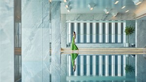 Una piscina interior moderna con superficie reflectante, paredes de mármol y diseño minimalista.