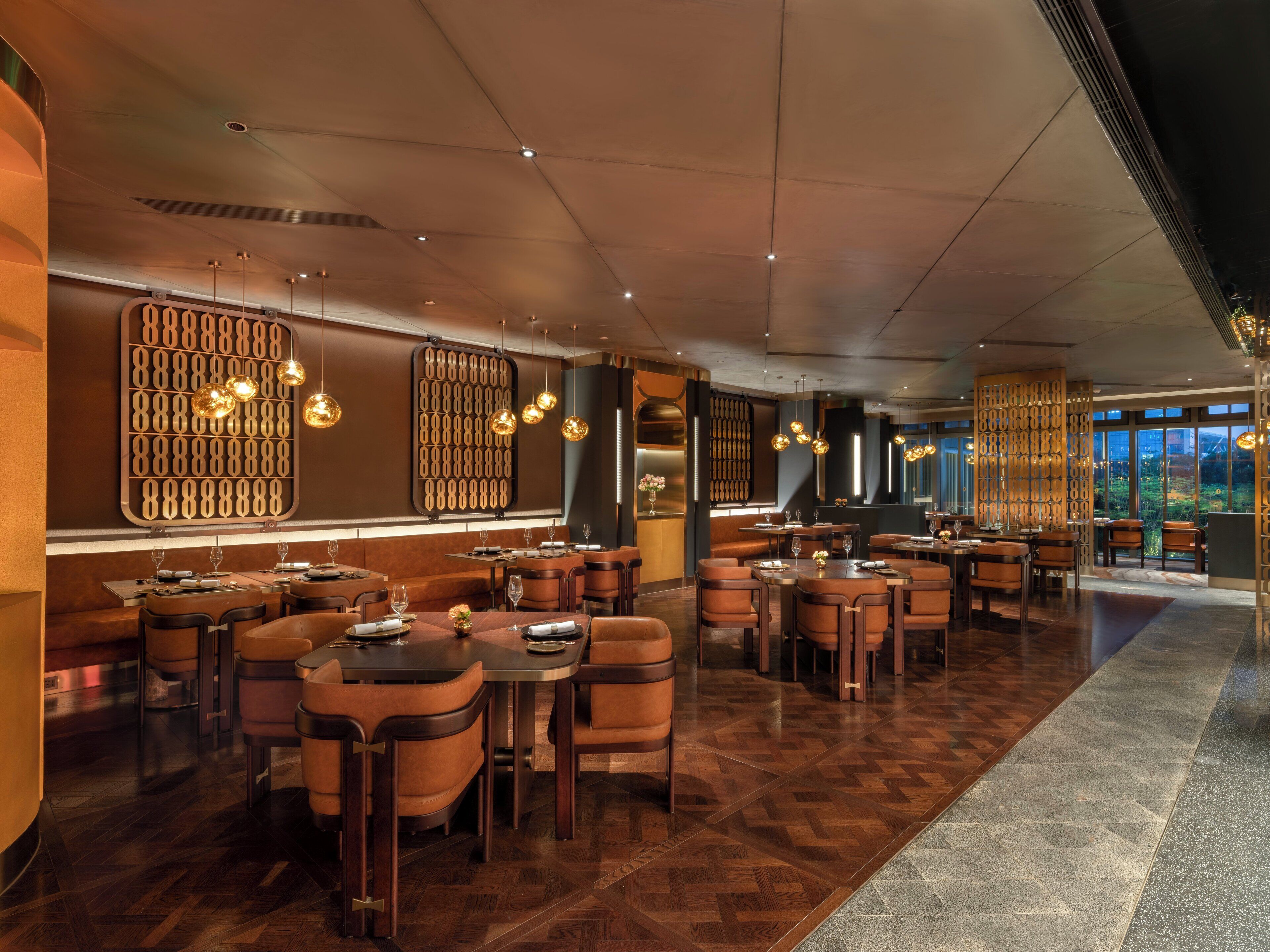 A modern restaurant with wooden flooring, brown leather chairs, and pendant lighting. Tables are set with wine glasses and plates.