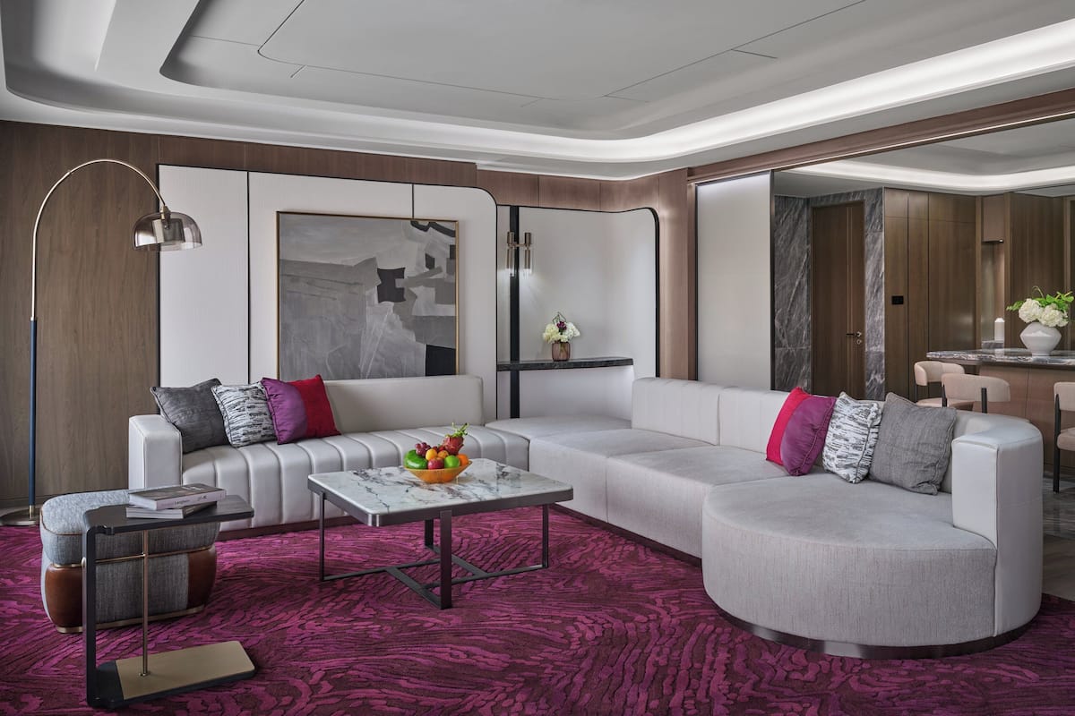 Una sala moderna con un sofá modular, una mesa de centro y una lámpara de pie. Hay un cuadro en la pared y un florero con flores sobre una mesita auxiliar.