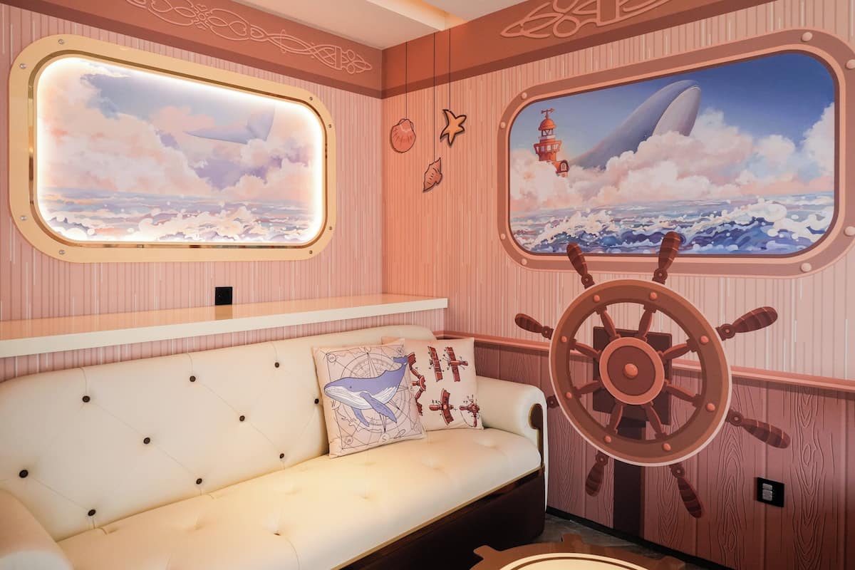 Una habitación temática náutica, que incluye un sofá con un cojín de ballena, una rueda de barco y murales marinos.