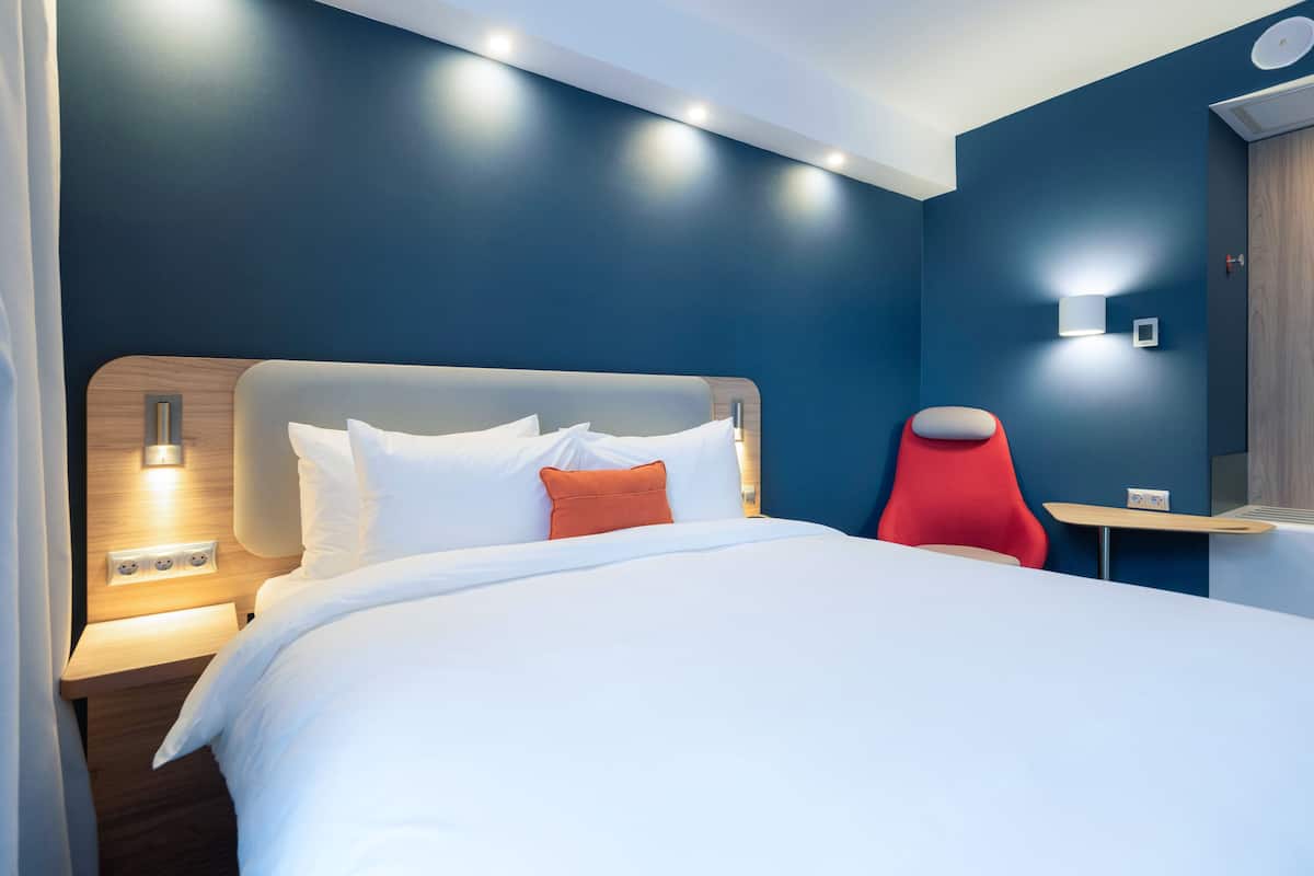 A modern hotel room with a large bed, a red chair, and a small table.
