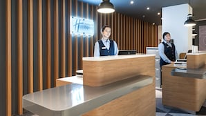 Uma área de recepção de hotel moderna, com painel de parede de madeira, balcão de recepção e tela digital.