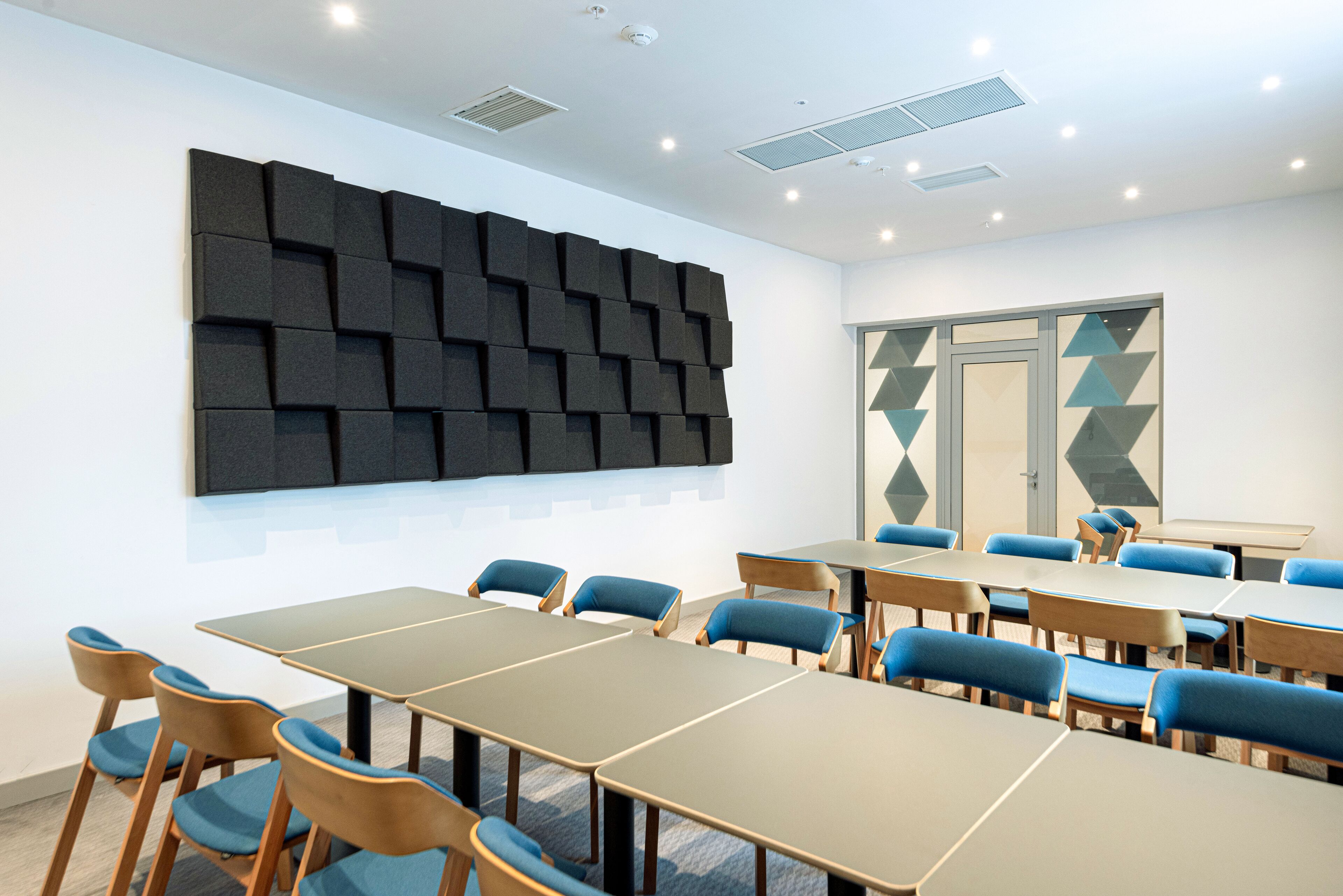 Un salón de conferencias de diseño moderno, con un gran muro insonorizado, sillas tapizadas en azul y un adorno mural geométrico.