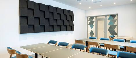 Un salón de conferencias de diseño moderno, con un gran muro insonorizado, sillas tapizadas en azul y un adorno mural geométrico.