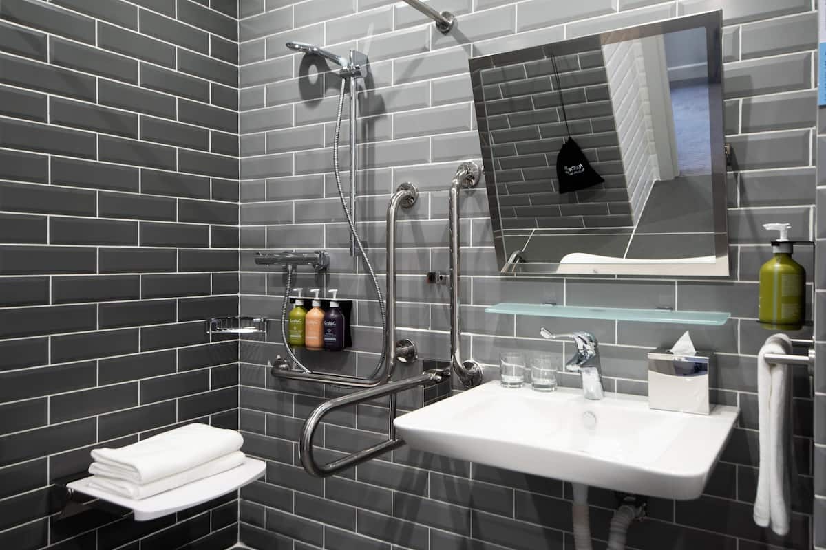 A modern bathroom with a grey-tiled wall, a white sink, a glass shower enclosure, and a mirror above the sink.