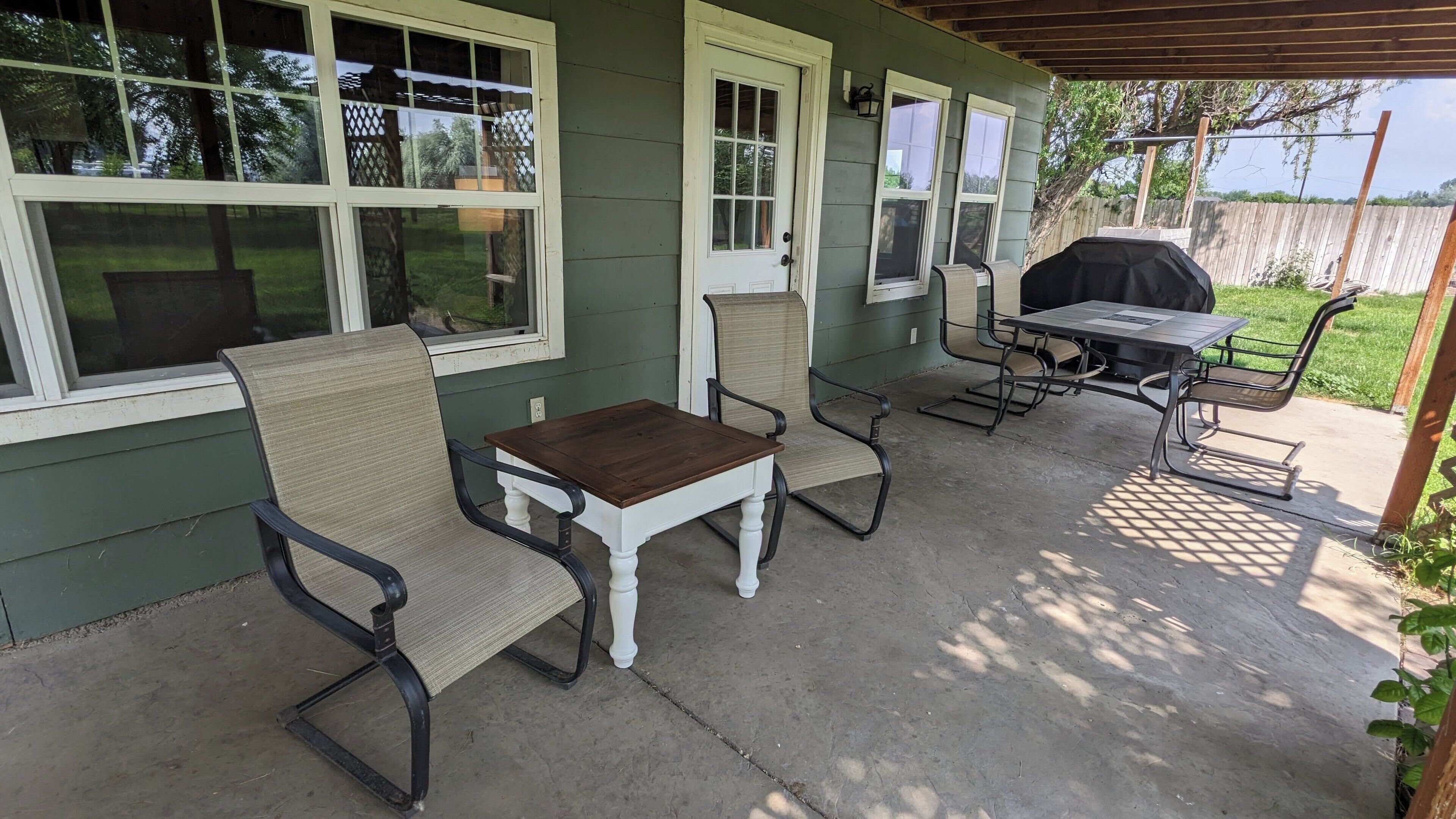 Un patio couvert aménagé avec du mobilier d’extérieur, notamment des chaises et une table, ainsi qu’un barbecue.
