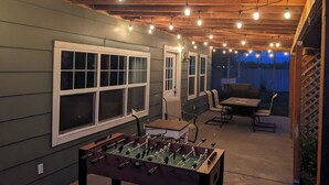 Un espace extérieur aménagé en patio, avec une table de baby-foot, des sièges et des guirlandes lumineuses.