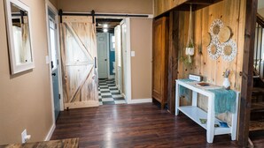 Un intérieur en bois avec un sol à carreaux, une console blanche sur laquelle est posé un panneau d’accueil et un escalier.