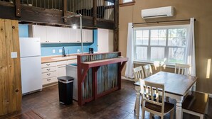 Une cuisine avec un escalier en bois, des placards blancs, une table à manger avec des chaises et une fenêtre avec des rideaux.