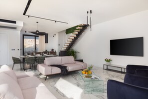Uma sala de estar moderna com um sofá, uma mesa de centro com frutas, uma televisão e uma escada com parede verde.