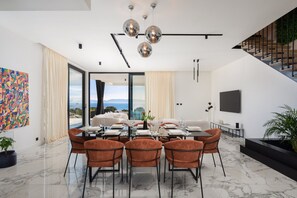Uma sala de jantar moderna com uma mesa grande, cadeiras laranja e vista para o mar.