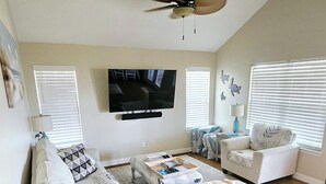 A spacious living room with a large sofa, a coffee table, and a television mounted on the wall. - Short walk to the beach (Freeport)