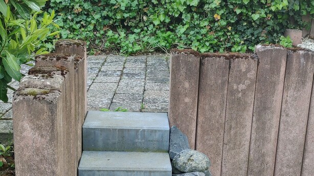 Un conjunto de escalones de piedra que conducen a una cerca de madera, rodeado de follaje.