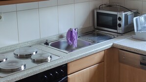 Una cocina con armarios de madera, estufa de acero inoxidable, horno, microondas y un ventilador pequeño.