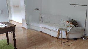 Una sala de estar moderna con un sofá blanco, una mesa de centro de vidrio, una mesa de comedor de madera y una alfombra verde.