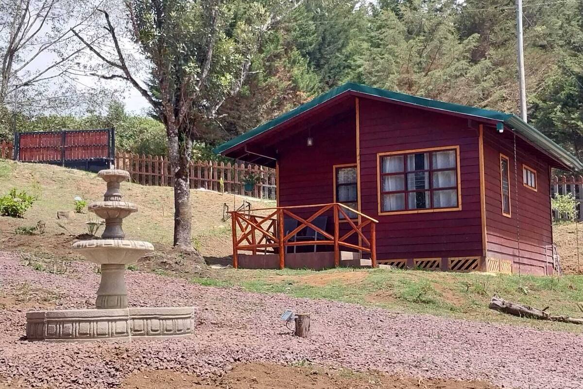 A small wooden cabin with a green roof, a stone fountain, and a wooden deck.