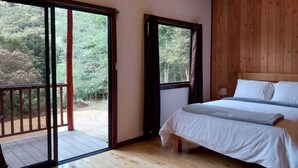 Une chambre avec un plancher en bois, un lit avec une literie blanche et une vue sur l’extérieur grâce à une porte coulissante.