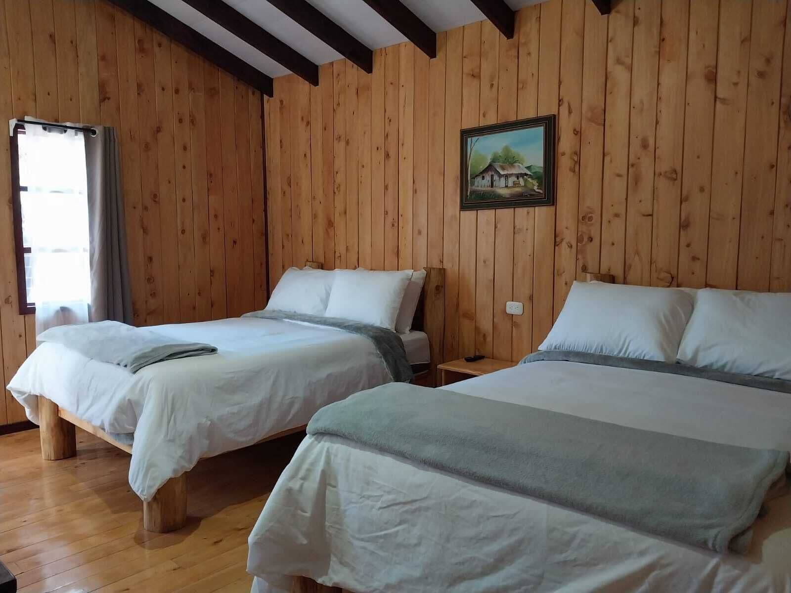 A room with two beds, wooden walls, a painting, and a window.