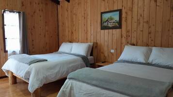 A room with two beds, wooden walls, a painting, and a window.