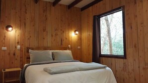 Une chambre à coucher aux murs lambrés, avec un lit, des tables de chevet et une fenêtre donnant sur les arbres.
