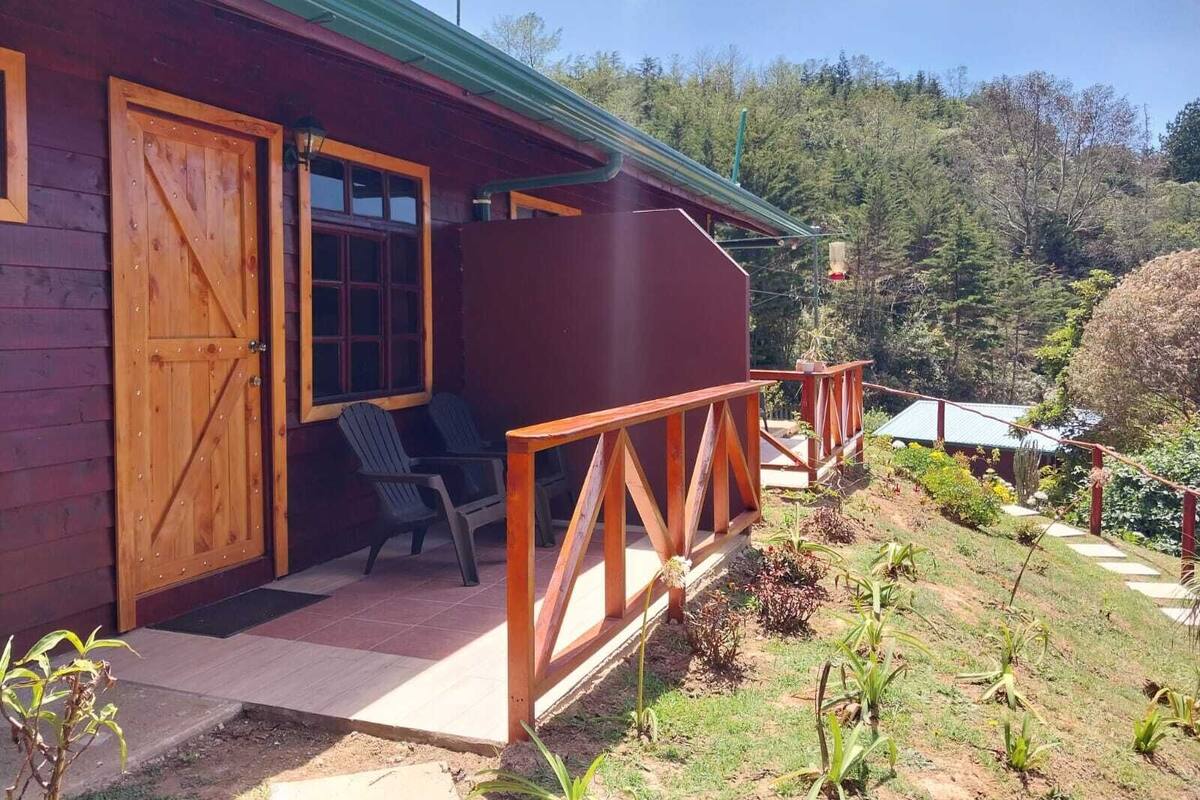 A wooden cabin with a porch, two chairs, and a small garden.