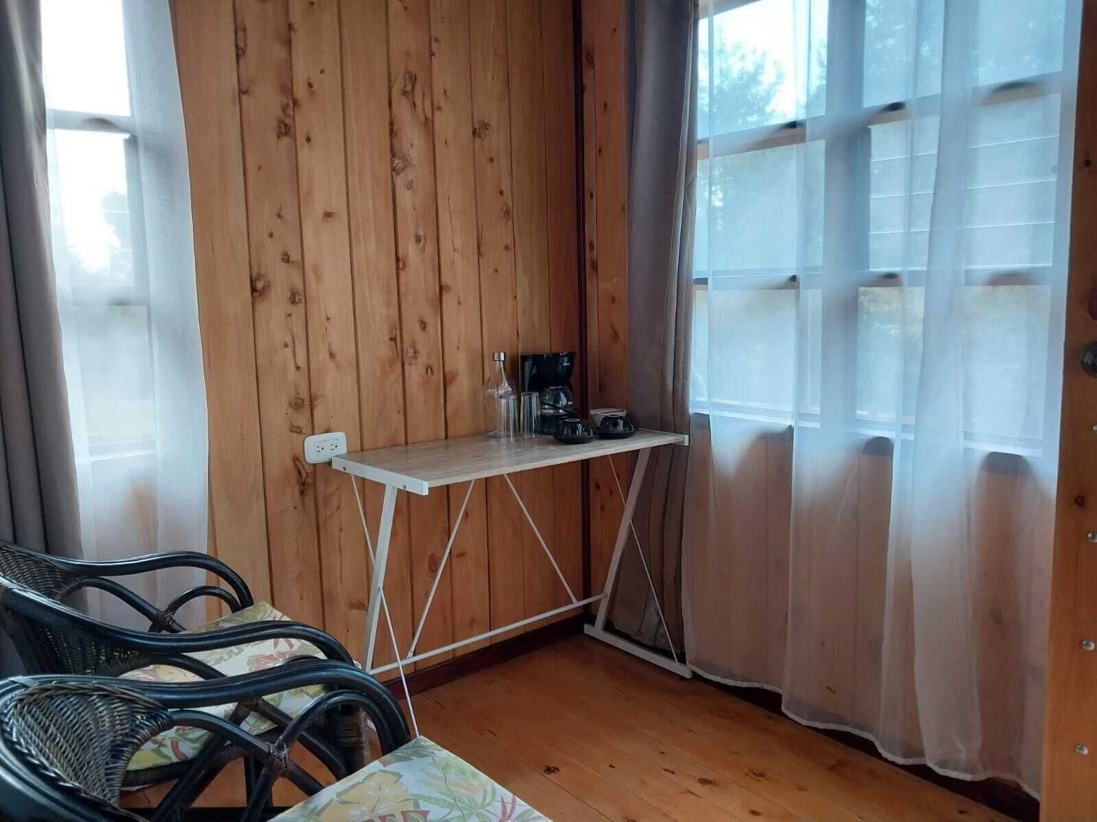 Ein kleines Zimmer mit Holzwänden, einem Tisch mit Kaffeemaschine und zwei Stühlen.