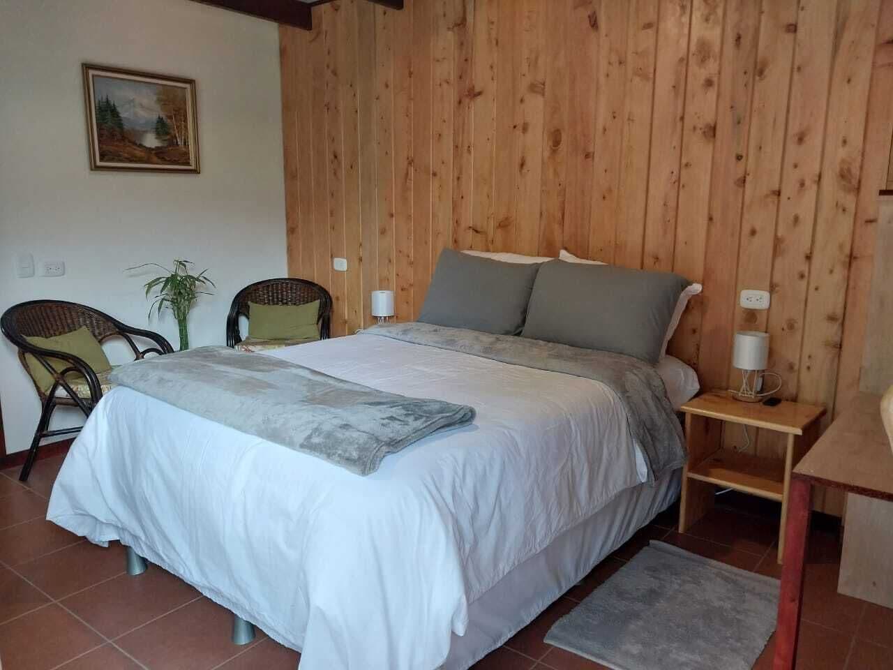 Ein Schlafzimmer mit einem großen Bett, zwei Stühlen, einem kleinen Tisch, einer Lampe und einem Gemälde an der Wand.