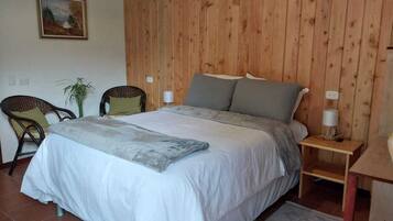 Ein Schlafzimmer mit einem großen Bett, zwei Stühlen, einem kleinen Tisch, einer Lampe und einem Gemälde an der Wand.