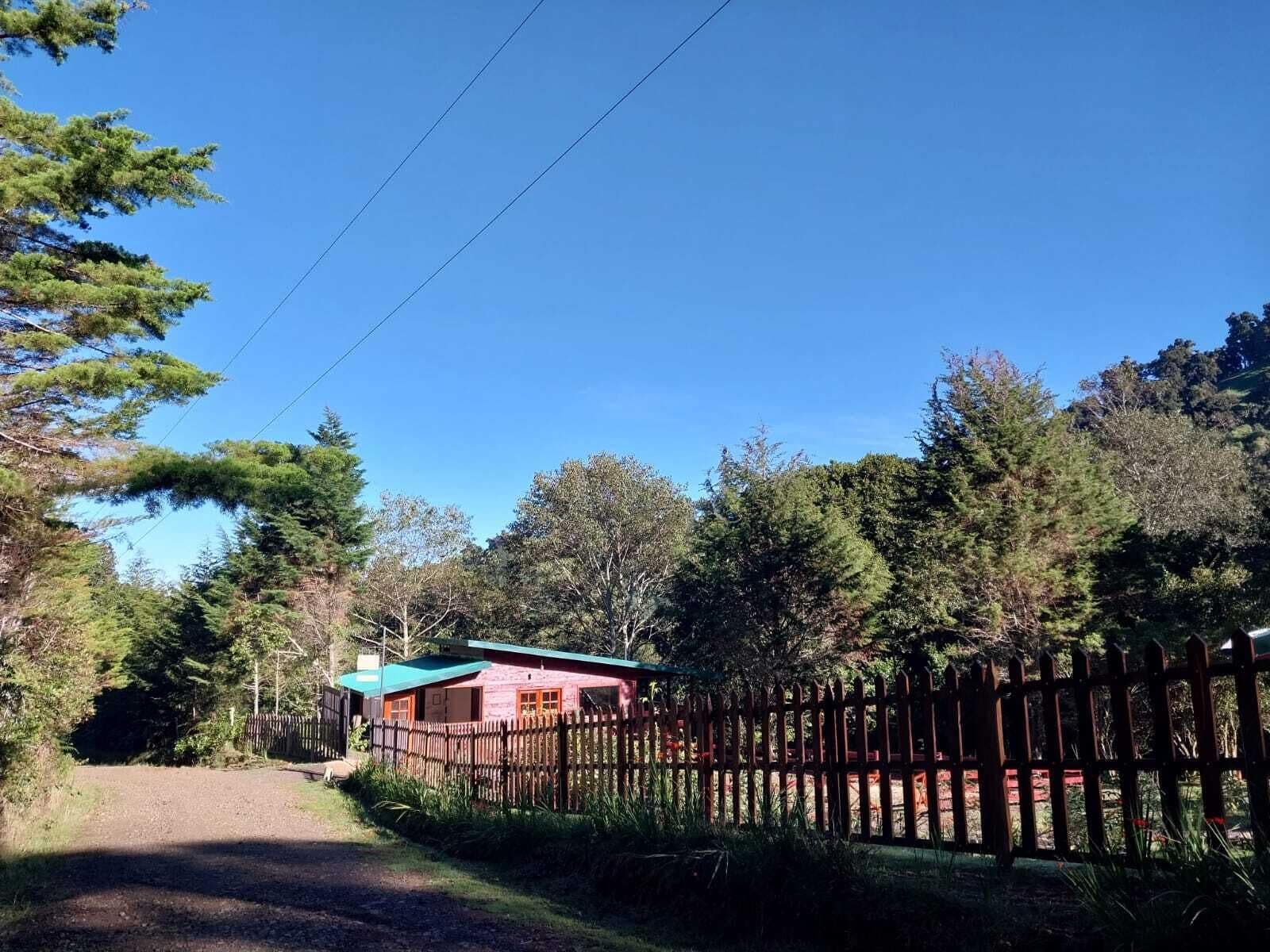 A rural setting with a wooden fence, a gravel path, and a small building with a green roof.