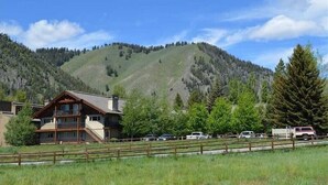 A two-story lodge with a balcony, surrounded by a fenced parking area and a mountainous backdrop. - Sun Valley/Ketchum-Location, Hot tub, pet friendly, walk to ski and downtown (Ketchum)