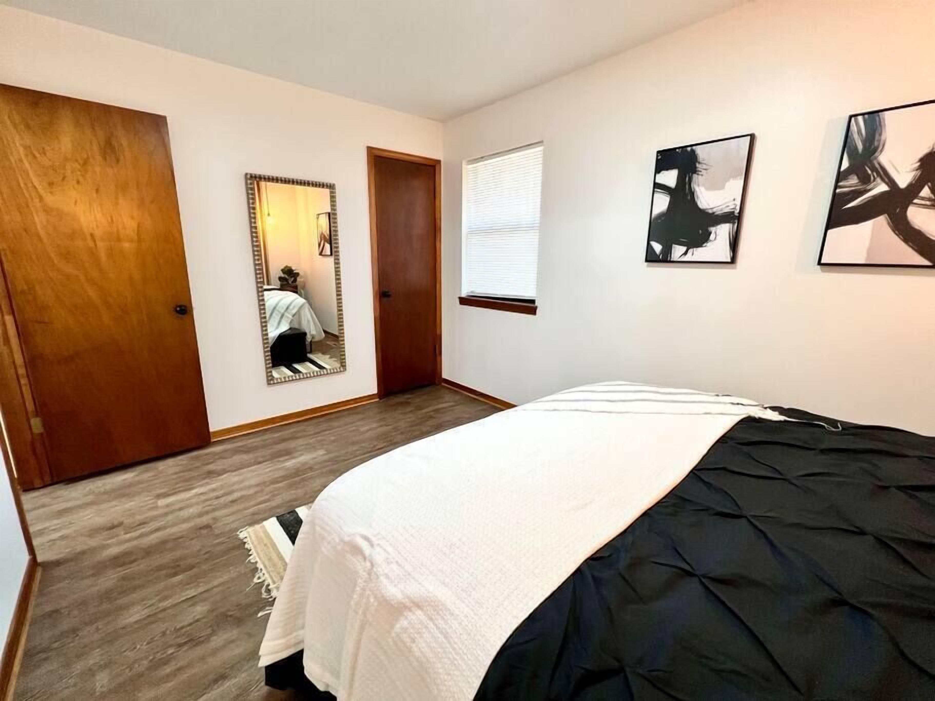 A bedroom with a bed, a wooden door, a mirror, and two wall-mounted artworks.