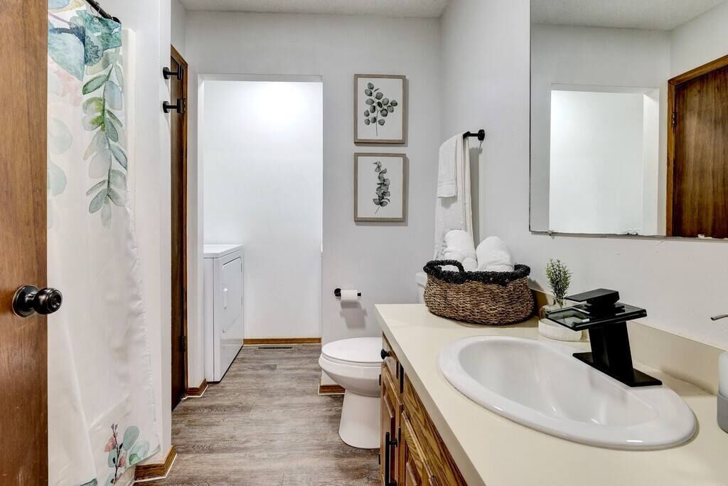 A bathroom with a white sink, wooden cabinets, a white toilet, and two framed wall art pieces.