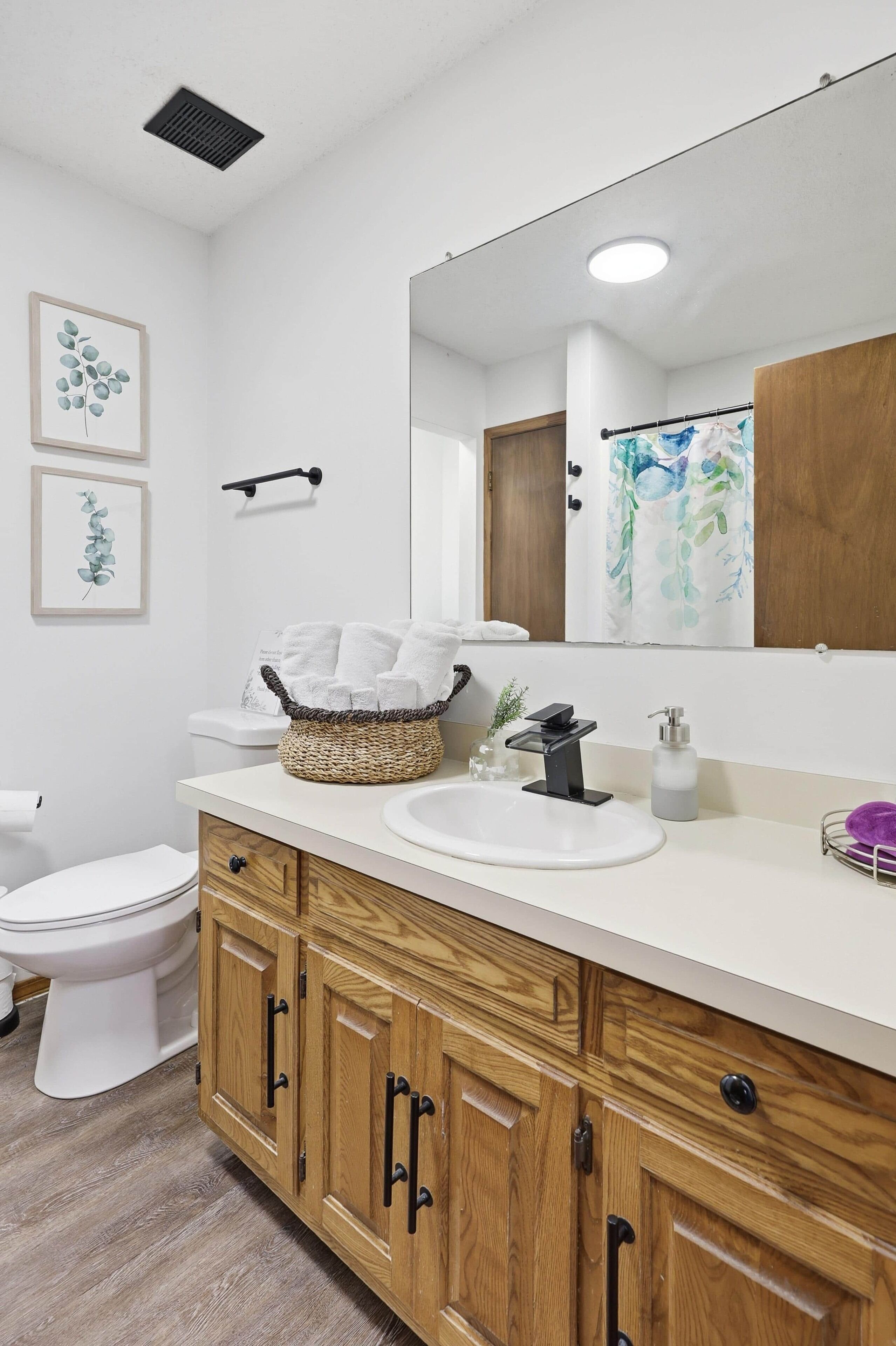 A modern bathroom with a wooden vanity, white sink, and a large mirror.