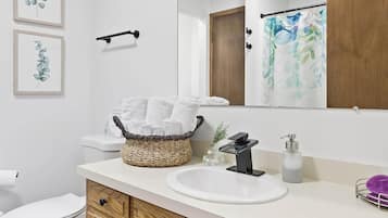 A modern bathroom with a wooden vanity, white sink, and a large mirror.