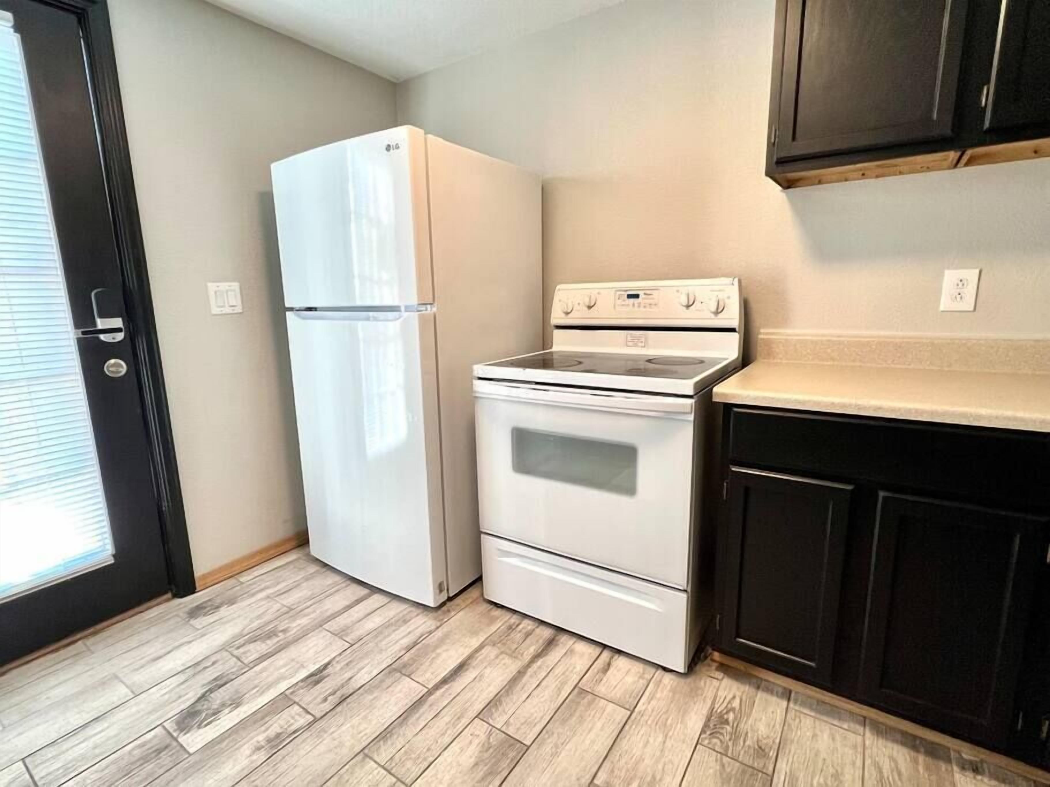 Una cocina compacta con refrigerador, estufa y gabinetes oscuros.