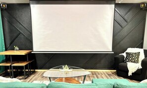 A room with a large projection screen, a wooden coffee table, a black armchair, and a green sofa.