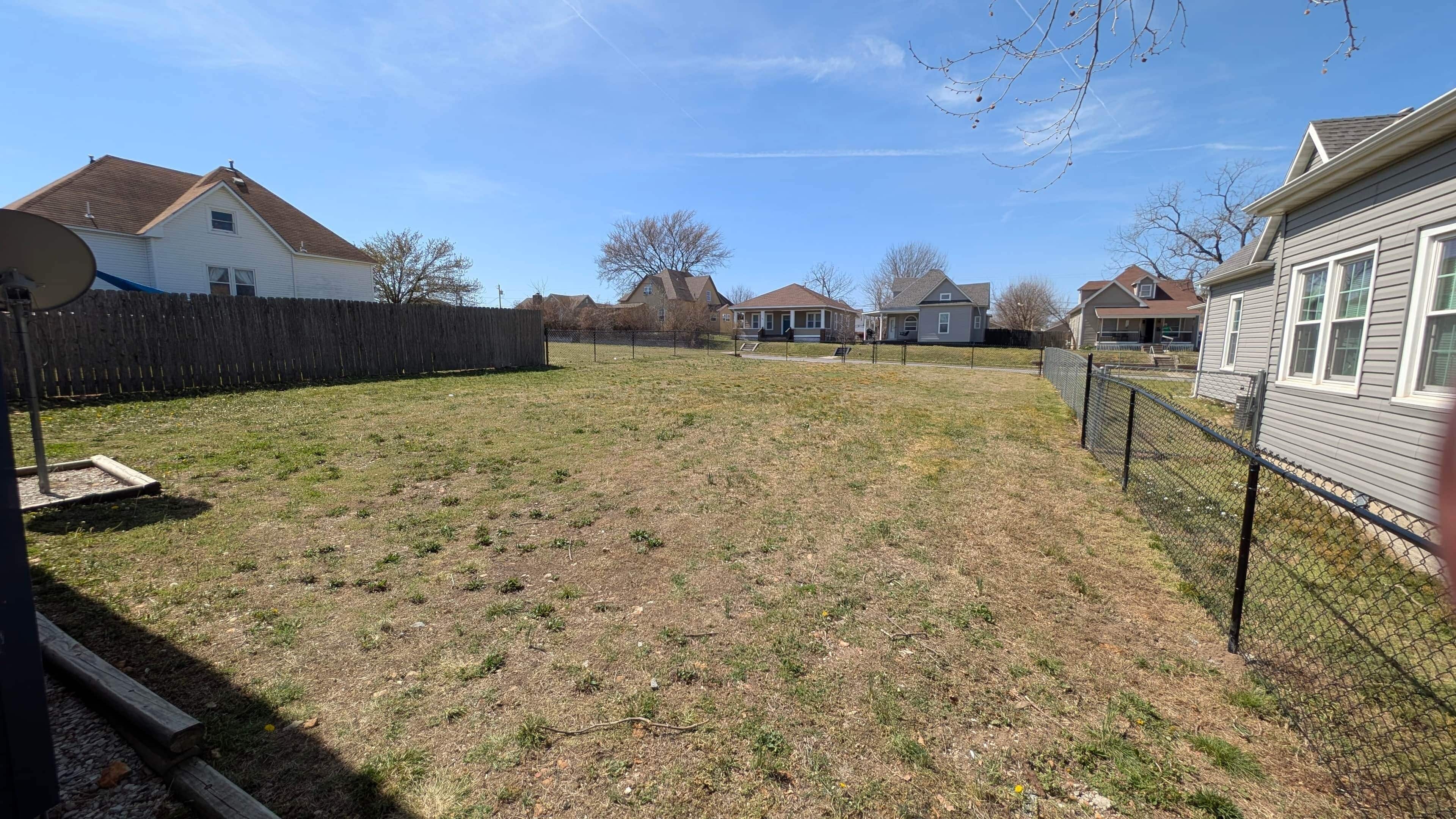 A residential backyard with a fenced area, a satellite dish, and houses in the background.