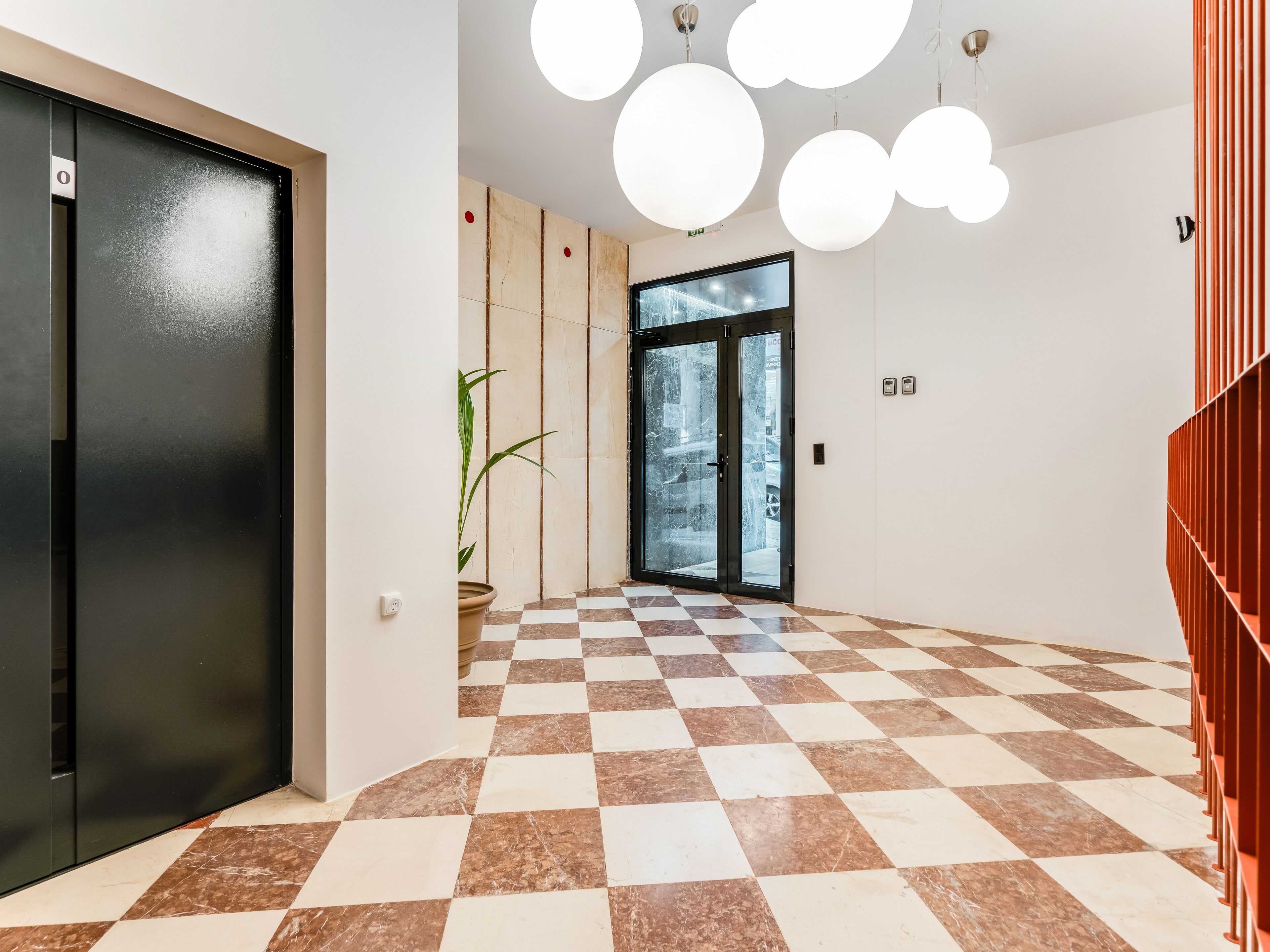 A hallway with a checkered floor, a potted plant, a door with a number, and a glass door with a view of the outside.