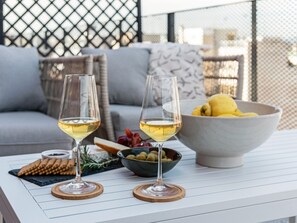 Two wine glasses on a white table with a bowl of fruit and olives, a plate of crackers, and a cheese board. - Sanders Port - Sleeky Studio With Roof-top Terrace (Piraeus)