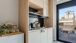 Una cuina moderna amb armaris blancs, una papereta d'acer inoxidable i ampolles de vi. Una porta corredissa dona pas a un balcó amb vistes a edificis.