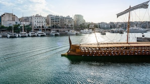 Un port amb diverses embarcacions amarrades, una barca de fusta al primer pla i edificis al fons.