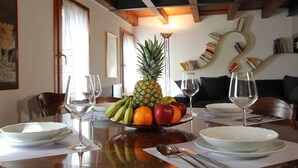 A dining table with a fruit bowl, wine glasses, and plates, set in a room with wooden beams and a bookshelf. - Frari Prestige Canal View (Historical Center) (Venecia)