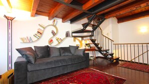 A modern living room with a grey sofa, a red patterned rug, a spiral staircase, and bookshelves. - Frari Prestige Canal View (Historical Center) (Venecia)