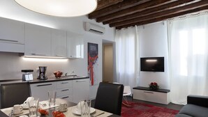 Un salon moderne comprenant un coin repas, un téléviseur à écran plat et une cuisine avec des meubles blancs et une machine à café.