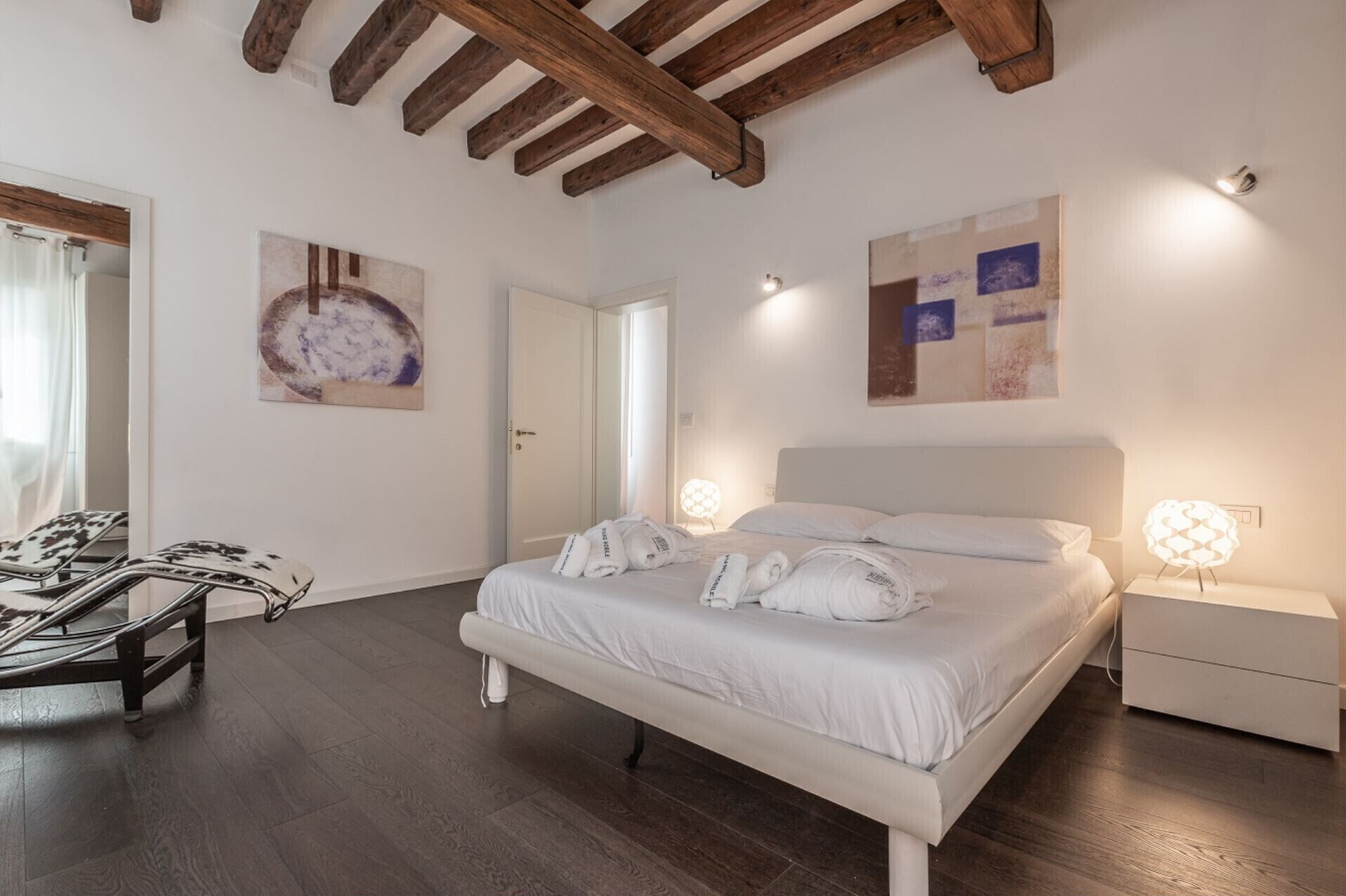 Un dormitorio moderno con una cama grande, vigas de madera en el techo y obras de arte en las paredes.