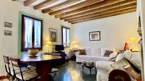 Una sala de estar acogedora con techo de madera, un sofá blanco, una mesa de comedor con sillas y un televisor.