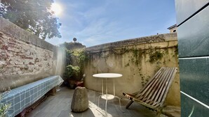 Un patio con un banco de piedra, una mesa redonda y una silla de madera.