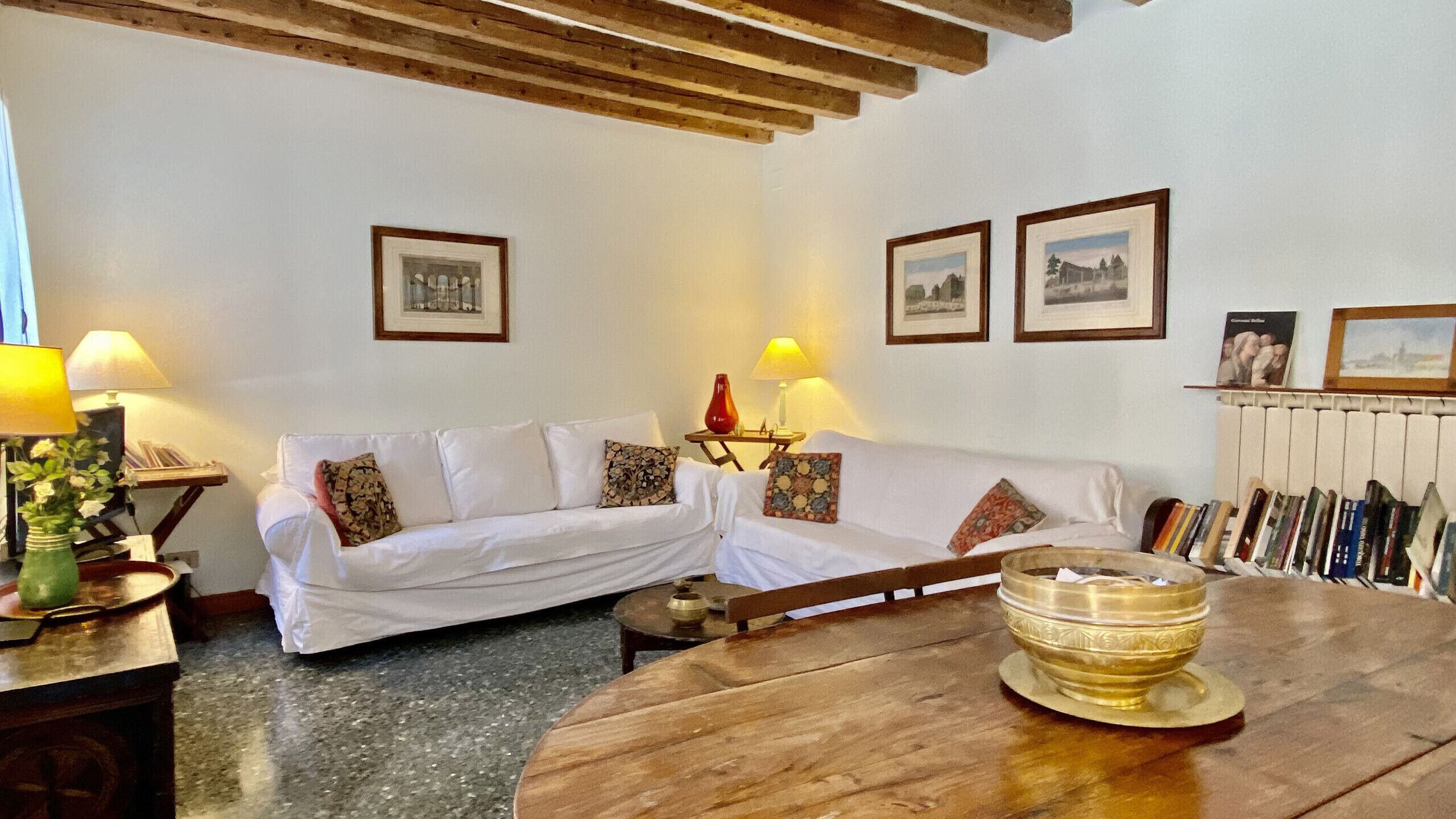 Una sala de estar acogedora con una mesa de madera, dos sofás blancos y un radiador.