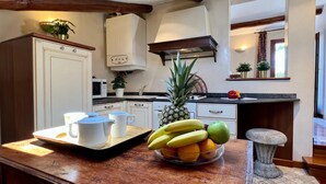 Une cuisine avec des meubles blancs, un four à micro-ondes, une cuisinière et un panier de fruits posé sur le comptoir.