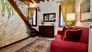 Une pièce chaleureuse avec un canapé rouge, une commode en bois, un miroir et un escalier dont le mur est décoré de motifs floraux.